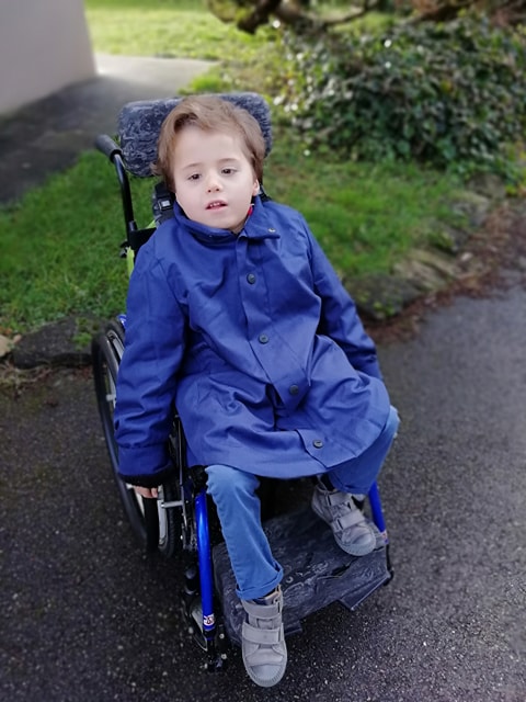 Antonin, en situation de handicap et fauteuil roulant, porte le manteau ALBA bleu